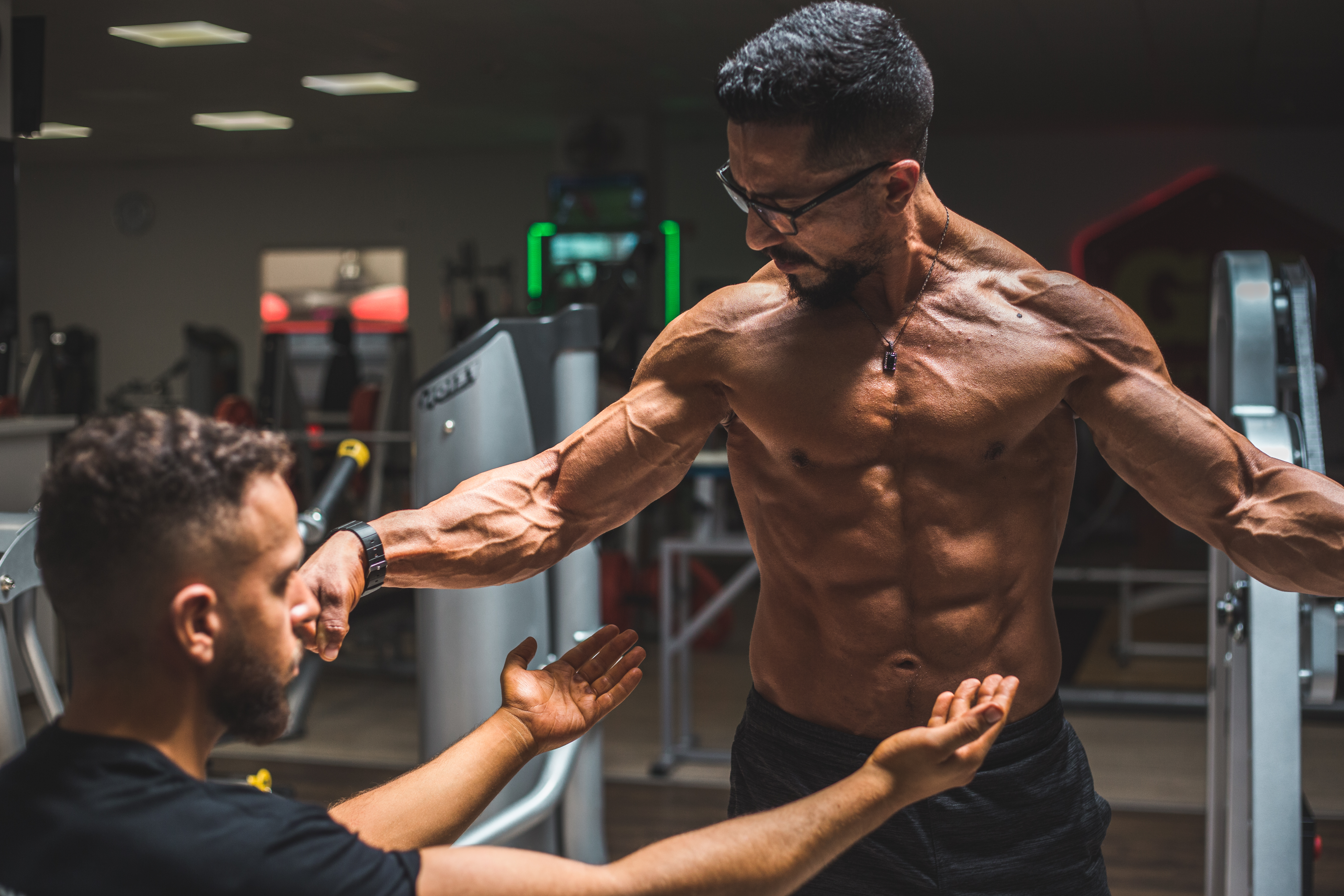A muscular fitness coach instructing a client in a gym.